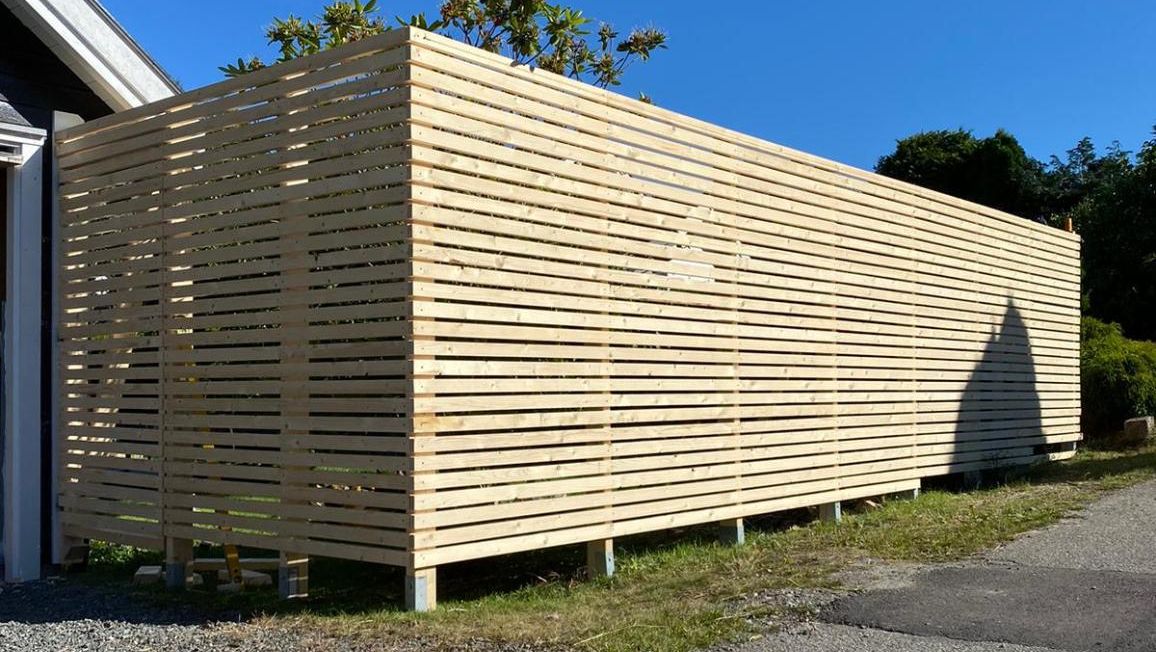 Nyoppført levegg i tre med horisontale spiler. Viser ferdigstilt snekkerarbeid på uteområde.