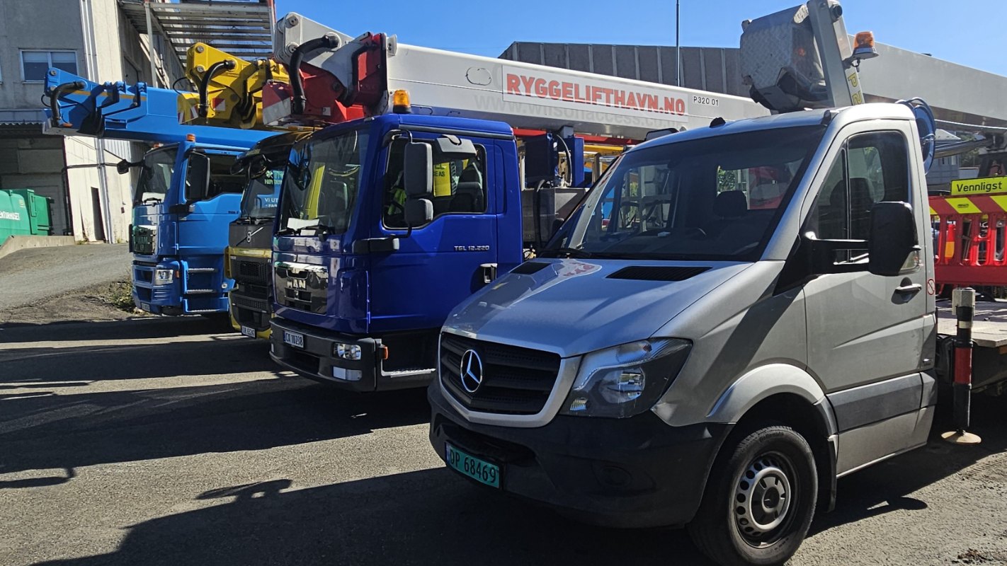 Liftbil med lang arm utfører arbeid over tak på bygg ved havneområde.